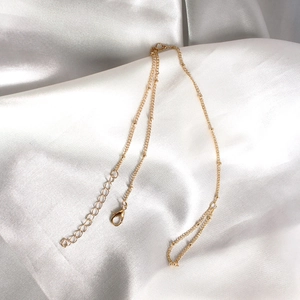 Détail d'une chaîne à billes dorée avec fermoir mousqueton sur tissu de soie blanc
