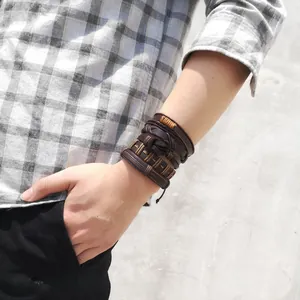 Detail of layered brown braided leather bracelets with leaf charms on male wrist