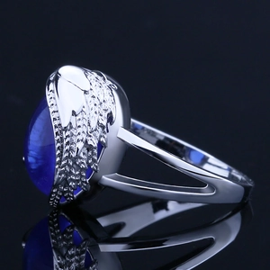 Silver angel wing ring featuring an oval blue sapphire gemstone on a black reflective surface
