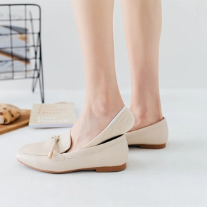 Women's beige loafers with metal bow buckle and no-show socks in a minimalist setting
