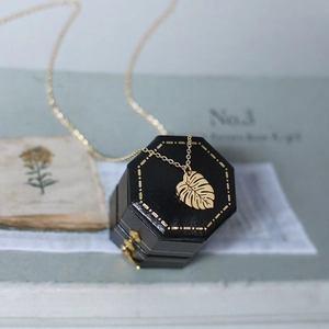 Golden monstera leaf necklace in a black gift box with minimalist tropical palm design