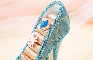 Macro detail of teal high heel jewelry holder with champagne satin slots and pink flower
