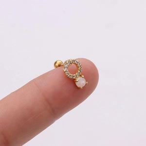 Vue macro d'un clou d'oreille en opale et zircon doré posé sur le bout du doigt