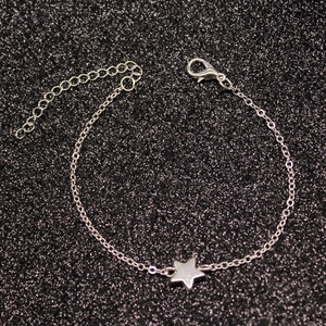 Detail shot of silver star charm bracelet with lobster clasp on black glitter background