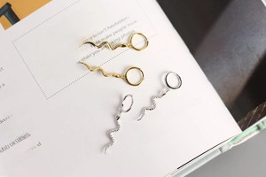 Detailed flat lay of silver and gold snake drop earrings on an open book background