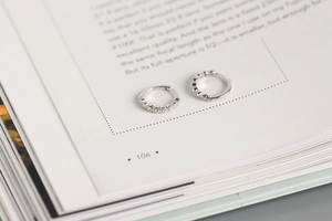 Macro detail of silver S925 hoop earrings with clear crystals on an open book