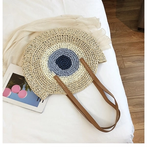 Détail du sac de plage rond en paille tressée avec motifs bleus et anses en cuir élégantes
