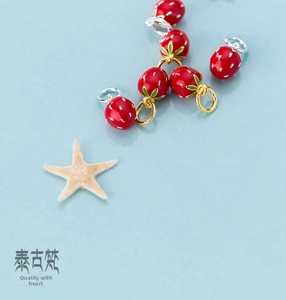Macro shot of red enamel strawberry charms for DIY jewelry making on blue background