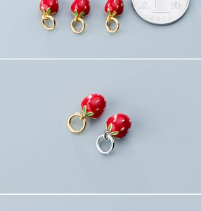 Detail of red strawberry pendants with gold and silver loops next to a coin for scale