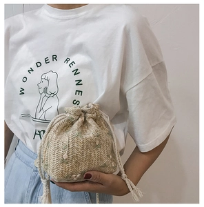 Detail of hand-woven straw bucket bag featuring delicate floral embroidery and drawstring