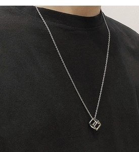 Close-up of a silver hollow cube pendant necklace worn on a model against a grey wall