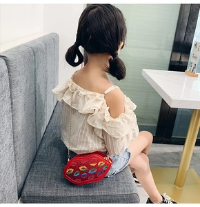 Detailed view of red lip-shaped kids crossbody bag with glitter and metal chain strap