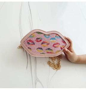 Detail of child hand holding a pink glitter lip-shaped crossbody bag with gold chain