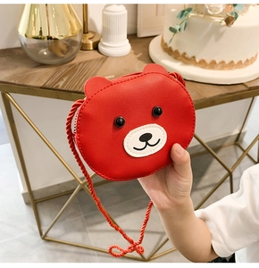 Close-up of red PU leather bear crossbody bag with woven rope strap held by hand