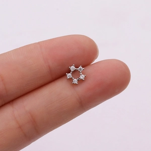 Macro shot of silver flower tragus stud with clear zircon on a finger tip