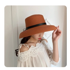 Detailed view of a brown straw sun hat with black ribbon worn by a model in a lace top