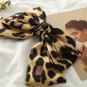 Detail of satin leopard print bow hair clip with textured fabric on white background