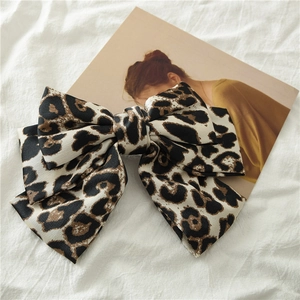 Detail of satin leopard print bow hair clip on a soft white linen fabric background