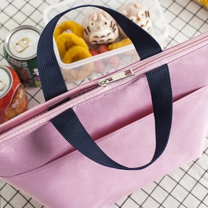 Pink insulated lunch bag with navy blue handles on a white grid tablecloth setting