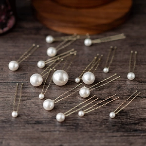 Detailed view of U-shaped hair pins with glossy pearls on a rustic wooden surface