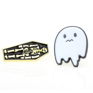 Detailed shot of coffin skull enamel pin and white ghost brooch set on white background