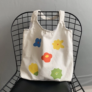 Dettaglio della borsa tote in tela bianca con cinque motivi floreali colorati su una sedia