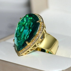 Macro detail of gold teardrop ring featuring a large green crystal and diamond halo