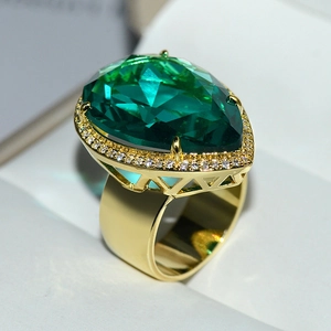 Close-up of golden ring with large green teardrop crystal and small diamond halo