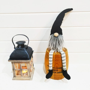Christmas gnome doll with black hat and gray beard sitting on a barrel in cozy home decor