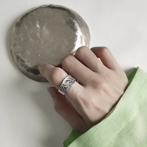 Detail of wide S925 sterling silver ring with irregular hammered rock texture on finger