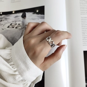 Detail of silver crisscross geometric ring worn on finger against fashion magazine background