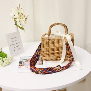 Detail of hand-woven straw bag with colorful geometric strap and silk bow on a table