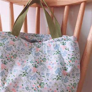 Detail der floralen Canvas-Tasche mit grünen Tragegriffen an einem Holzstuhl hängend