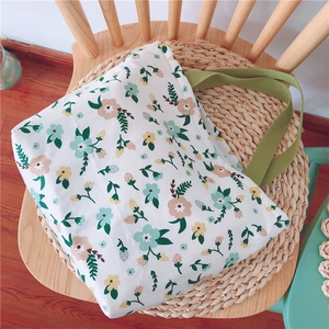 Florale Canvas-Lunchtasche mit grünen Griffen auf rustikaler Webmatte auf Holzstuhl