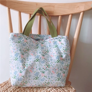 Detail einer floralen Baumwolltasche mit grünen Griffen auf einem Holzstuhl