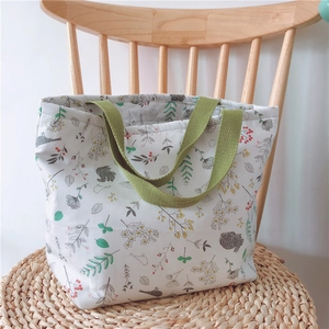Detail der floralen Canvas-Lunchtasche mit grünen Griffen auf einem Holzstuhl