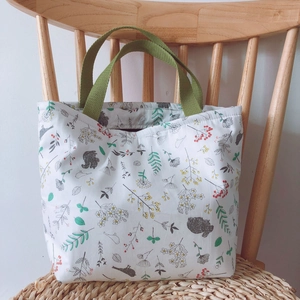 Blumige Canvas-Lunchtasche mit grünen Griffen auf Holzstuhl, natürlicher Stil