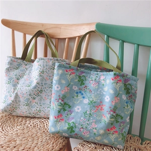 Florale Canvas-Tragetaschen in Weiß und Hellblau mit grünen Griffen auf Holzstühlen