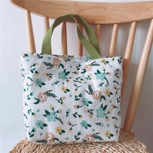 Nahaufnahme einer kleinen Stofftasche mit Blumenmuster und grünen Griffen am Holzstuhl