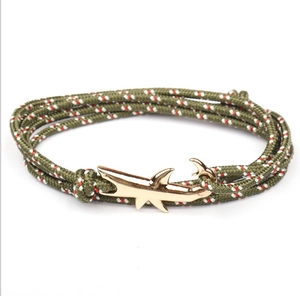 Detail of army green woven rope bracelet with a gold-colored shark-shaped metal clasp