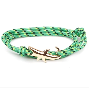 Macro detail of green woven rope bracelet featuring a golden shark shaped metal buckle clasp
