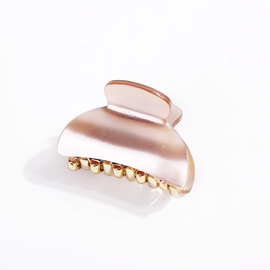 Detail of pearlescent pink acrylic hair claw clip with golden metal comb teeth structure