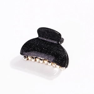 Close-up of a black acrylic claw clip with gold glitter finish and golden teeth detail