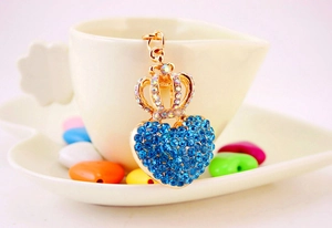 Detail of golden crown and heart keychain with blue rhinestones on a white cup