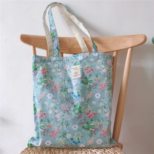 Floral canvas tote bag in light blue with pink blossom prints hanging on wooden chair