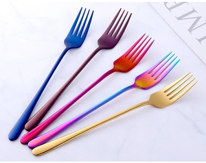 Close-up of set of five colorful stainless steel steak forks on white marble surface