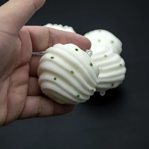 White spiral textured Christmas ornament ball with green glitter dots held in hand