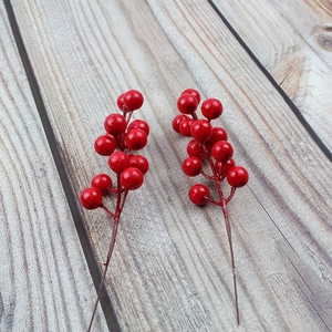Detailed view of two artificial red berry stems on a light wood background for Christmas decor
