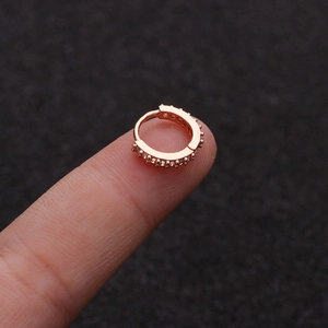 Macro shot of tiny rose gold zircon ear hoop resting on fingertip showing small scale