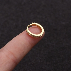 Macro shot of a small gold zircon hoop earring held on a finger to show the compact size